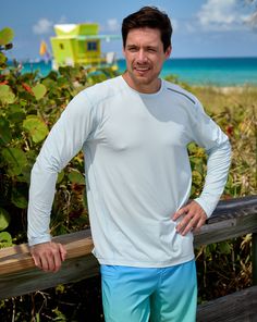 a man standing next to a wooden fence near the ocean with his hands on his hips