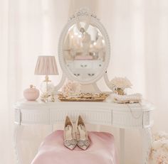 a white dressing table with a mirror and shoes on it next to a pink blanket