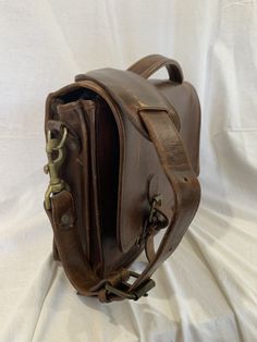 a brown leather bag sitting on top of a white sheet