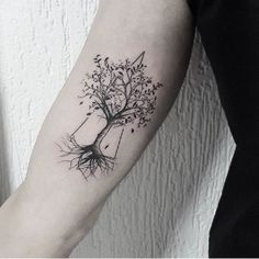 a black and white tree tattoo on the left arm, with roots growing out of it