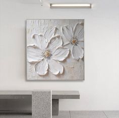 a white flower painting hanging on the wall next to a concrete bench in an empty room