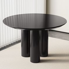 a black round table sitting on top of a rug next to a white wall with vertical blinds