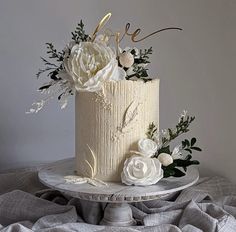 a wedding cake with white flowers and greenery sits on a tablecloth covered surface