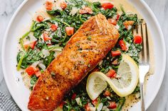 a plate with salmon, spinach and lemon wedges on it next to a fork