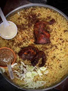 a pan filled with rice and meat next to two bowls of dipping sauces on the side