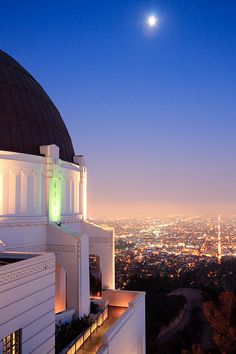 the moon is seen over the city lights and dome on top of an old building