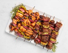 a white plate topped with meat and veggies on top of a wooden skewer