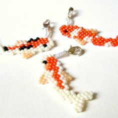 three beaded charms are displayed on a white surface, one is orange and the other is black