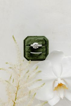 an engagement ring sitting on top of a green velvet box next to a white flower