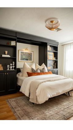 a white bed sitting under a window next to a book shelf filled with books and pillows