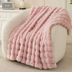 a white chair with a pink fluffy blanket on it's back and the seat up