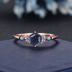 a blue diamond ring sitting on top of a black book with flowers in the background