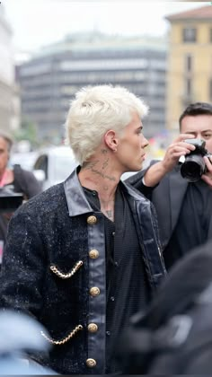 a man with white hair and tattoos taking a photo in front of a group of people