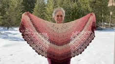 a woman is holding up a crocheted shawl in the snow