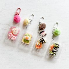 small plastic containers with food in them on a white surface, one has a keychain and the other is a bag charm