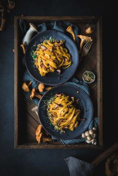 two plates of pasta with mushrooms and parmesan cheese on the side next to a fork