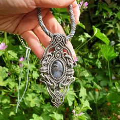 a hand holding a silver necklace with a stone in the center and an intricate design on it