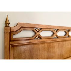 a wooden headboard with metal finials on the top and bottom posts, against a white wall