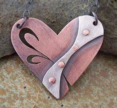 a wooden heart with pink and white designs hanging from it's side on a chain