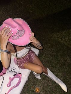 a woman sitting on the ground wearing a pink hat and holding her hands up to her face