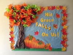 a bulletin board decorated with fall leaves and a pumpkin on the ground next to a tree