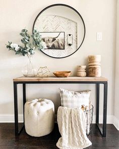 a white and black console table with a mirror on the wall next to pillows, vases and other decorative items