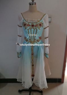 a white and blue dress on a mannequin with gold trim around the neck