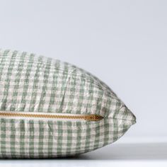 a green and white gingham pillow with gold zipper on the front, sitting on a white surface