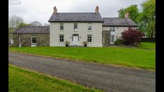 a white house sitting on the side of a road next to a lush green field