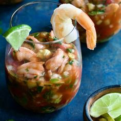 two glasses filled with shrimp and limeade garnished with cilantro on a blue surface