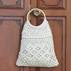 a crocheted white purse hanging on a wooden door with a metal ring in front of it