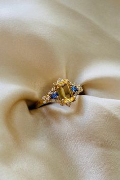 an engagement ring with blue and yellow sapphires sits on a white satin surface,