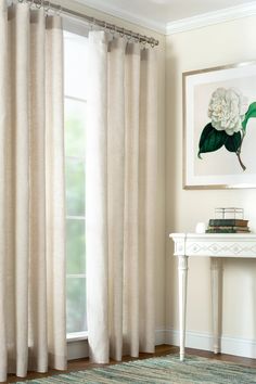 a living room with white curtains and a painting hanging on the wall above a table