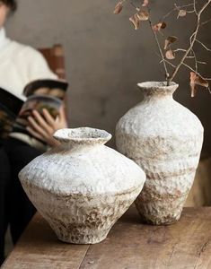 two white vases sitting on top of a wooden table next to a person holding a book