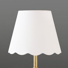 a lamp with a white shade on it sitting in front of a gray wall and floor