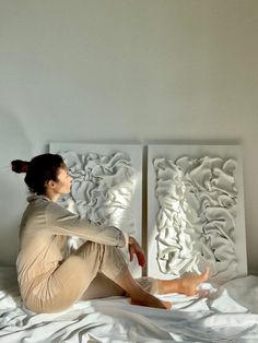 a woman sitting on top of a bed in front of two white wall art pieces