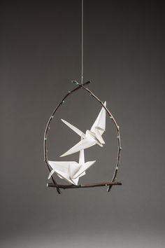 two white origami birds hanging from a twig in a circular frame on a gray background