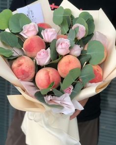 a person holding a bouquet of flowers and peaches with leaves on it's stems