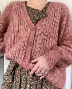 a woman is wearing a pink cardigan sweater and floral dress with her hands in her pockets