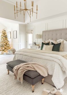 a bedroom decorated for christmas with a large bed and white carpeted flooring, gold chandelier