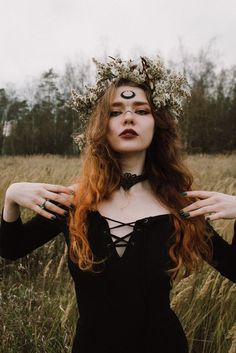 a woman with long red hair wearing a crown and black dress standing in tall grass