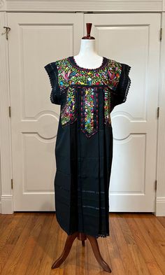 Mexican black dress is made with hand embroidery and multicolor silk threads by Zapotecs from Oaxaca Mexico. APPROXIMATE MEASUREMENTS. Around bust 50" Shoulder to bottom hem 46" PC # B-821 Made With 100% hand embroidery. 100% Artisanal Made. Imported Made in Oaxaca Mexico No two are alike-different embroidery patterns/colors Handmade, Boho, bohemian, Mexico, Hippie, Embroidery, Vintage, Huipil, Tunic, One of A Kind. Artisan Made, Ethnic Floral, Vintage Style. Black Bohemian Dress With Intricate Embroidery, Black Embroidered Short Sleeve Maxi Dress, Embroidered Black Maxi Dress With Short Sleeves, Black Short Sleeve Embroidered Maxi Dress, Black Dresses For Cinco De Mayo Fiesta, Black Bohemian Embroidered Dress For Festival, Black Bohemian Dress With Embroidered Neckline, Traditional Black Dress For Cinco De Mayo, Black Floral Embroidered Dress For Festival