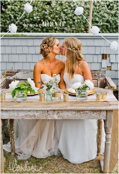 two women sitting at a table kissing each other