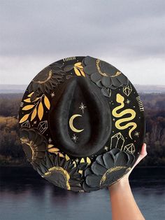 Halloween hat Brim is about 3.75" wide  Content: Vegan Suede Adjustable to fit your head better if needed  Elevate your style with this stunning hand-painted wide-brim fedora, crafted from luxurious vegan suede in a timeless black and gold palette. This one-of-a-kind piece is adorned with intricate designs featuring a serpent winding gracefully around the crown, sparkling crystals, celestial stars, delicate leaves, and a crescent moon. Each flower is meticulously painted with thick, textured strokes, adding a unique tactile dimension to the hat's sophisticated design. This fedora isn't just a hat; it's a wearable work of art. Perfect for making a statement at festivals, special events, or just adding a touch of magic to your everyday outfits. Whether you're dressing up or down, this versat Adjustable Flat Brim Costume Hat, Adjustable Flat Brim Halloween Costume Hat, Adjustable Flat Brim Halloween Hat, Adjustable Fedora Felt Hat For Halloween, Fedora Hat For Halloween Costume Party, Adjustable Flat Brim Hat For Halloween, Halloween Fedora For Costume Party, Adjustable Brimmed Felt Hat For Halloween, Adjustable Wide Brim Felt Hat For Halloween