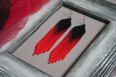 a pair of red and black beaded earrings hanging from a frame on a table