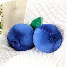 two blue fruit shaped pillows sitting on top of a white couch next to a plant