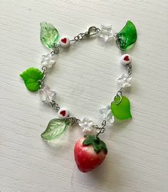 a bracelet with green leaves, red apple and clear glass beads on a white surface