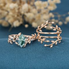 two gold rings with green and white stones in them on a blue surface next to flowers