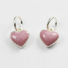 two pink heart shaped earrings on a white surface with silver bails and bead ends