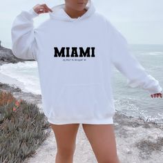 Introducing the perfect souvenir for your Miami trip - our Miami Hoodie! This stylish Miami Hoodie is a must-have for anyone who loves the city of Miami, Florida. Featuring a sleek and classic design, this hoodie is perfect for showing off your love for the city while still looking stylish. Made with high-quality materials, this Miami Hoodie is not only stylish but also comfortable to wear. Whether you're out exploring the city or just relaxing at home, this hoodie will keep you feeling warm and White Hooded Sweater With Letter Print, White Hoodie Sweatshirt With Letter Print, White Letter Print Hoodie Sweats, College Hooded Sweater With Letter Print, Long Sleeve Hoodie With Text Print For Loungewear, White Hooded Sweats With Letter Print, White Hooded Letter Print Sweats, White Hoodie With Letter Print For Loungewear, College Long Sleeve Hoodie With Slogan